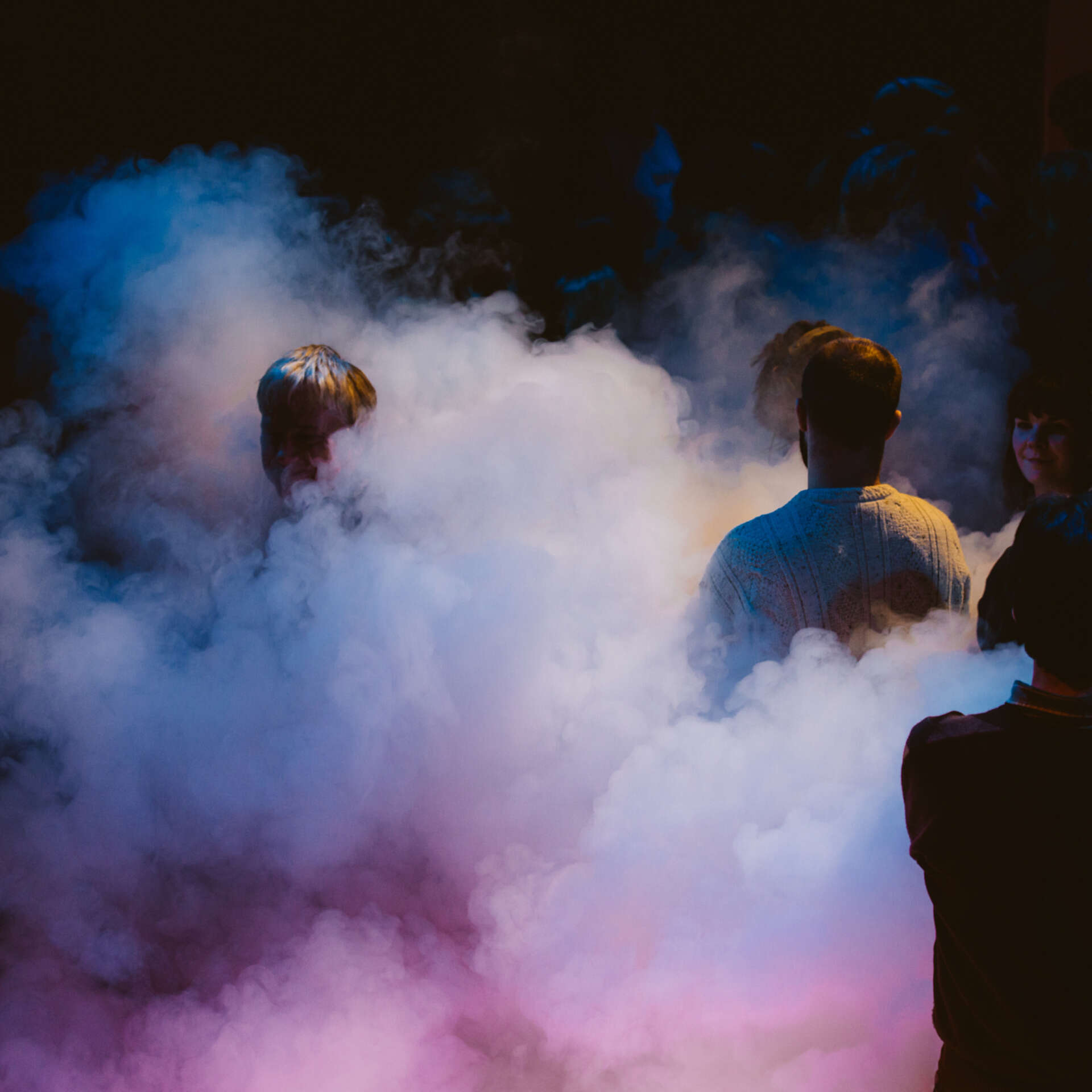 Performers are stood on stage with pink and purple smoke surrounding them.